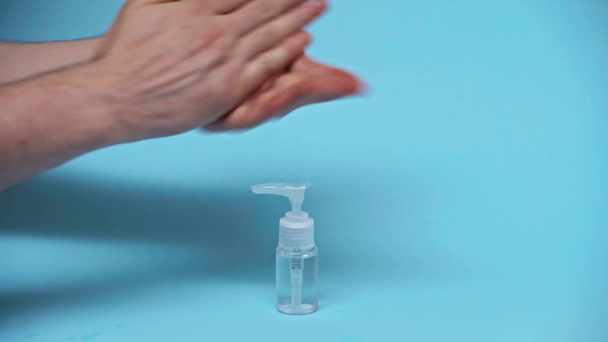 przycięty widok człowieka przy użyciu płynu antybakteryjnego w butelce na niebiesko  - Materiał filmowy, wideo