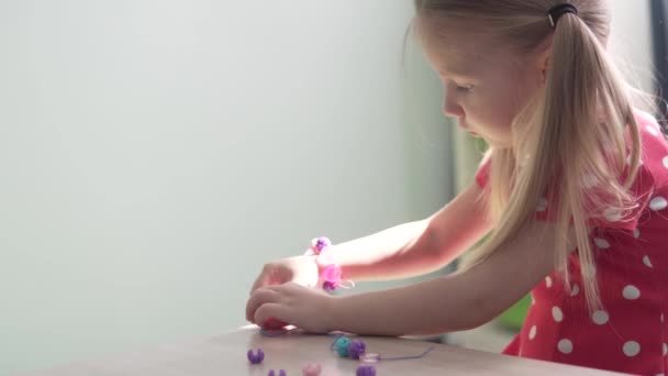 Een schattig meisje maakt een armband van een kinderen set voor handwerk - Video