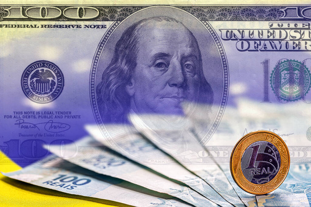 Brasilianisches Geld, Hundert-Dollar-Scheine und Ein-Real-Münzen, im Hintergrund ein Hundert-Dollar-Schein. Konzept des hohen Dollars, Krise in Brasilien. - Foto, Bild