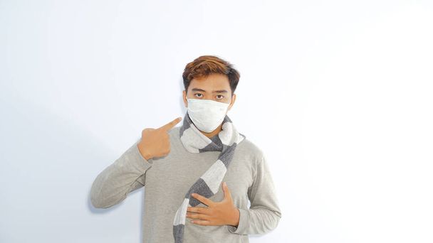 Effectieve bescherming tegen het coronavirus. Zieke Aziatische man draagt sjaal en wijst naar zijn maskers om mensen te overtuigen over een gezonde levensstijl en te voorkomen dat 2019-nCoV geïsoleerd over witte achtergrond - Foto, afbeelding