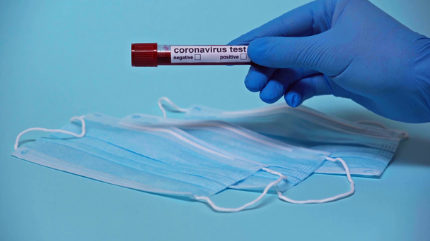 przycięty widok lekarza trzymającego próbkę koronawirusu w pobliżu masek medycznych na niebiesko - Materiał filmowy, wideo