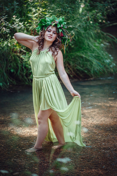 Piękna młoda kobieta w zielonej sukience i wieniec w słonecznym lesie. ceremonia w Święto Środka lub Ziemi. idea i koncepcja perfum, bajek i szczęścia - Zdjęcie, obraz