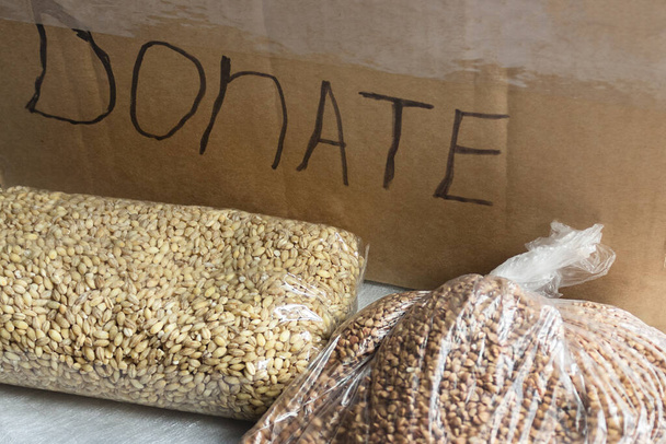buckwheat and oat groats lie on the background of a box with inscription "donate". Whole grain foods with high fiber content. Healthy diet ingredients, food delivery concept with copy space - Photo, Image