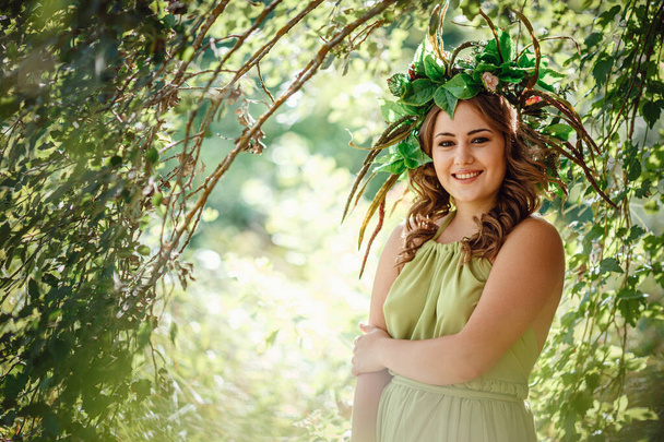 Krásná mladá žena v zelených šatech a věnec ve slunném lese. na slunovrat nebo na Den Země. myšlenka a koncept parfému, pohádek a štěstí - Fotografie, Obrázek
