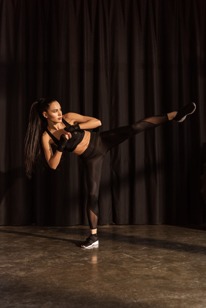 Привлекательная спортсменка пинается ногой на черном фоне
 - Фото, изображение