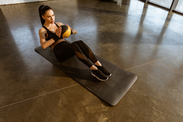 High angle view of sportswoman holding ball and doing abs on fitness mat in gym - Fotoğraf, Görsel