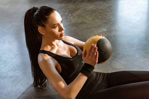 Sportswoman holding ball and doing abs in sports center - Foto, Imagem