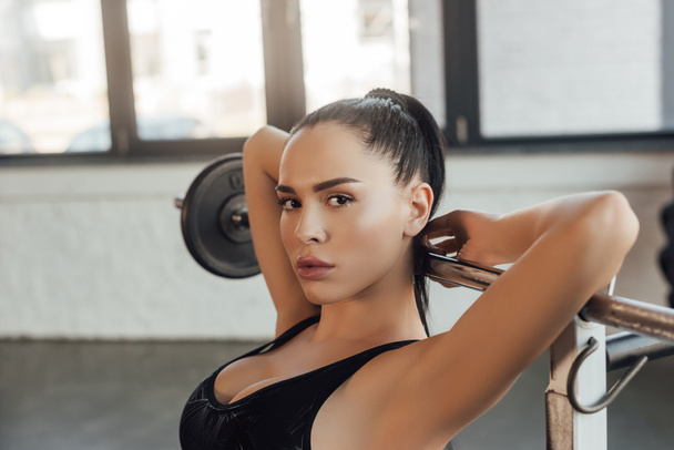 sexy sportswoman w pobliżu sztanga patrząc w kamery w siłowni - Zdjęcie, obraz