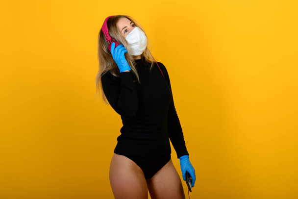 Portrait of a girl in a medical mask, which puts on a rubber glove. Yellow and grey background. Copy space. - Photo, Image