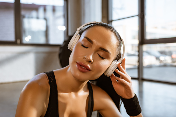 Портрет спортсменки с закрытыми глазами слушающей музыку в наушниках в тренажерном зале
 - Фото, изображение