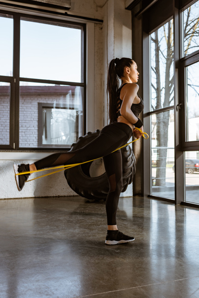 Side view of sportswoman working out with resistance band in gym - Photo, Image