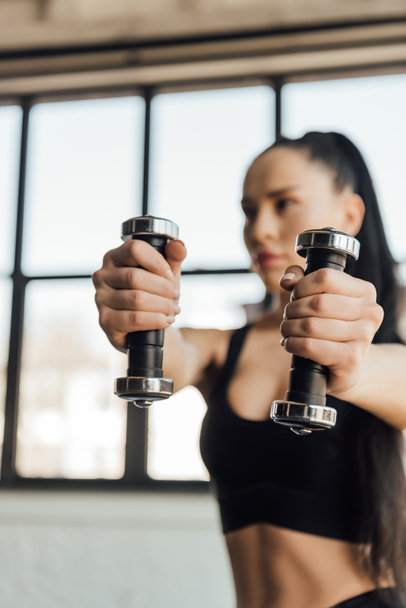 Selective focus of sportswoman holding dumbbells with outstretched hands in gym - Foto, Imagem