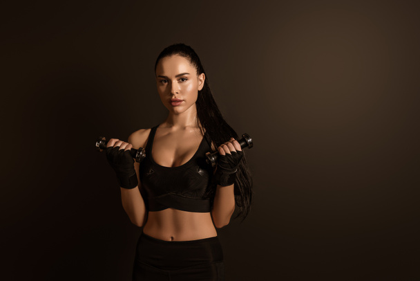 Sportswoman školení s činkami a při pohledu na kameru izolované na černé - Fotografie, Obrázek