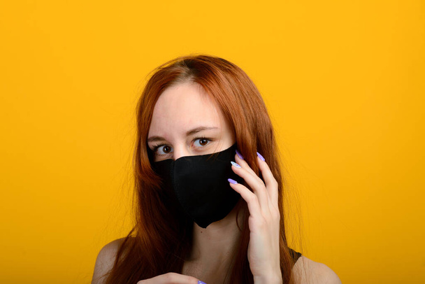 Portrait of a girl in a mask, which puts on a rubber glove. Yellow background. - Фото, изображение