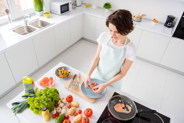 High angle above view photo of beautiful lady peel boiled shrimps cooking breakfast dinner prepared ingredients while red salmon frying grill pan wear apron modern kitchen indoors - Foto, imagen
