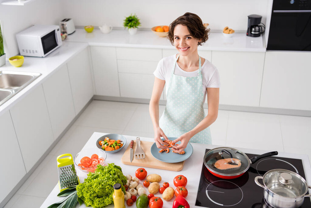 Photo of beautiful cheer housewife lady peel boiled shrimps cooking family dinner prepared ingredients red salmon frying grill pan healthy food wear apron modern kitchen indoors - Foto, afbeelding