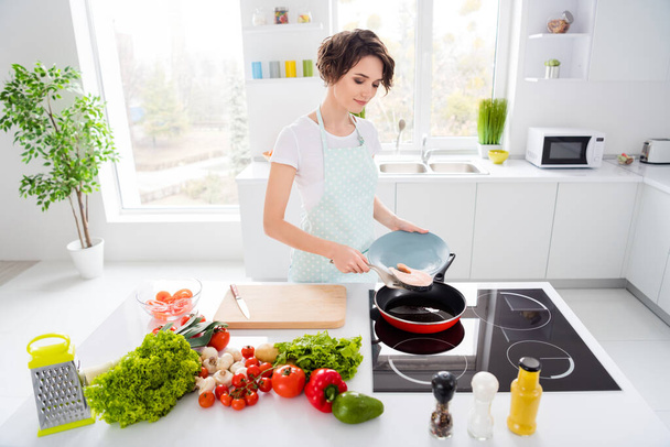 Photo of beautiful housewife lady putting fresh raw salmon fillet steak on flying pan keep diet morning cooking wear apron t-shirt stand modern utensils kitchen indoors - Fotó, kép