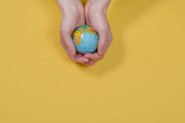 Globe in hands on a yellow background with copy space. The whole world is in your hands. Protect the world from war and disaster. Ecology problems. - Фото, изображение
