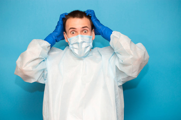 Portrait of scared man in protective suitt, medical mask and gloves against viruses and infections isolated on blue background. - Foto, Bild