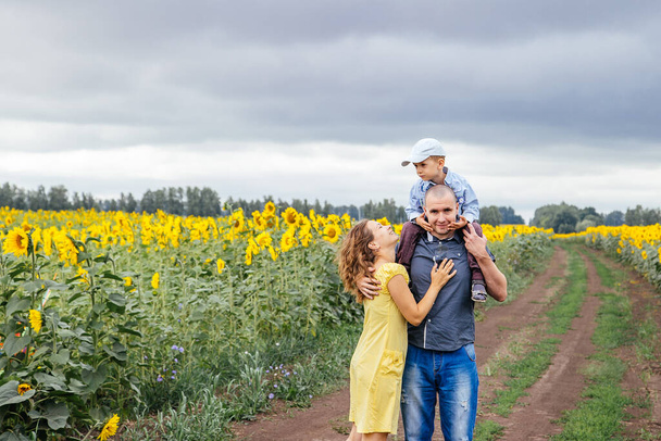 A young family of 3 people walking in a field of sunflowers. Rural area, Russia. - Foto, afbeelding