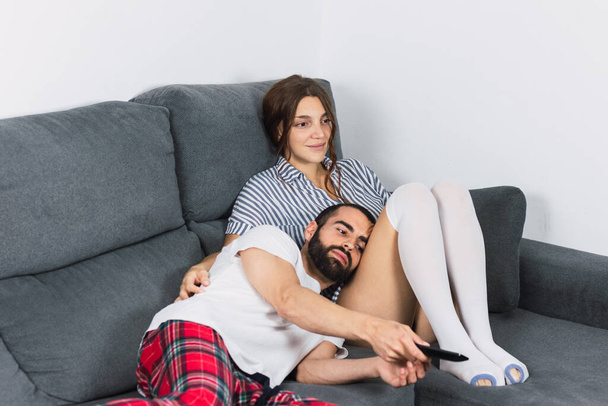 Χαλαρός νεαρή γυναίκα με τον άνδρα που αναζητούν τηλεόραση στον καναπέ στο σπίτι - Φωτογραφία, εικόνα