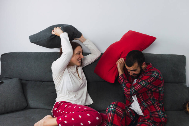 若いヒスパニック系のカップルが自宅でソファに座って、楽しさと質の高い時間を楽しんでいます。夫婦は枕の戦いをしている - 写真・画像