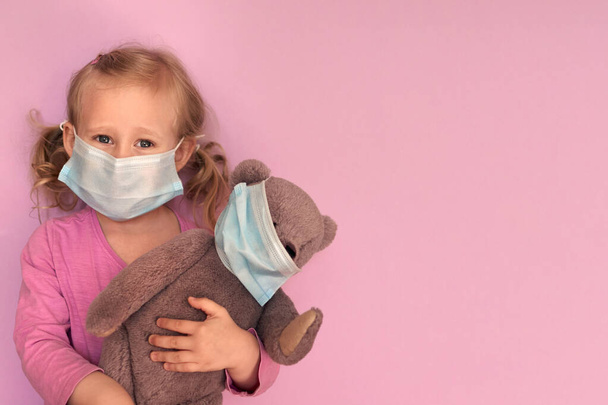 Dívka s medvídkem v masce. Kavkazské dítě nosí během epidemie koronaviru Covid-19 masku na ochranu obličeje. Zůstaň doma, společenská vzdálenost, izolovanost. během karantény. - Fotografie, Obrázek