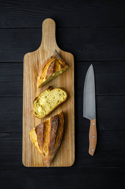Bread on a wooden board with a knife on a black background - Foto, imagen