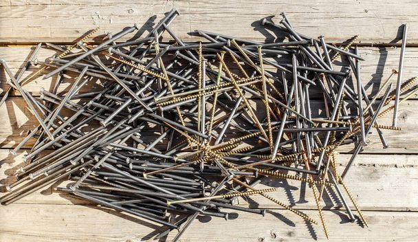 Iron nails and screws on a wooden background. Long, metal, carpenters nails and self-tapping screws for construction. Fixing tool. The view from the top. - Valokuva, kuva