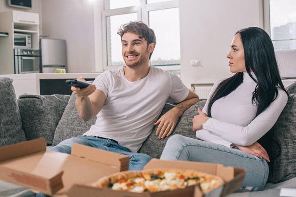 συναισθηματικό ζευγάρι έχοντας πίτσα και βλέποντας τηλεόραση με τηλεχειριστήριο κατά τη διάρκεια της αυτο-απομόνωσης στο σπίτι  - Φωτογραφία, εικόνα