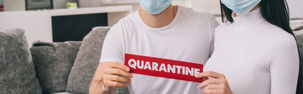 cropped view of ill couple in medical masks holding quarantine sign at home during self isolation, horizontal concept - Foto, Bild