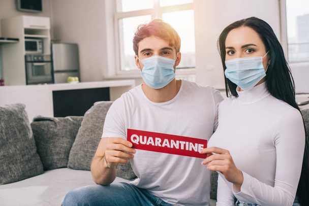 ill couple in medical masks holding quarantine sign at home during self isolation  - Foto, Imagem