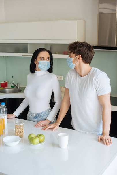 όμορφο ζευγάρι με ιατρικές μάσκες πρωινό στο σπίτι κατά τη διάρκεια της αυτο-απομόνωσης - Φωτογραφία, εικόνα
