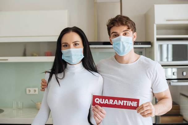 ill couple in medical masks holding quarantine sign at home during self isolation - Foto, Bild