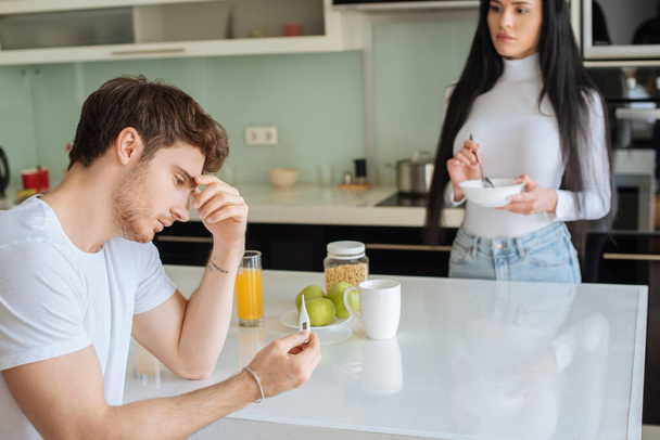 хворий чоловік тримає термометр, а жінка тримає миску зі сніданком вдома під час самоізоляції, вибірковий фокус
 - Фото, зображення