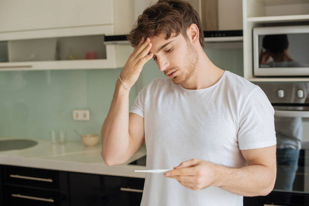 worried ill man looking at thermometer at home on self isolation  - Photo, Image