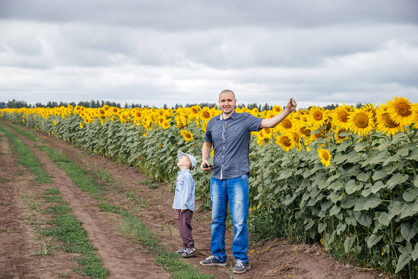 A father and son fly a kite in a field of sunflowers. Rural area, Russia. - Фото, изображение