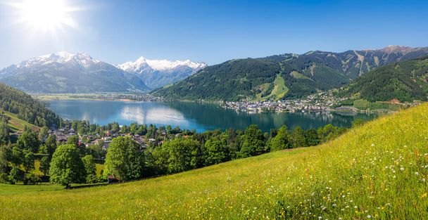 Сценічний панорамний вид красивих гірських краєвидів в Альпах з чистим озером і квітучими квітами на зелених луках в сонячний день з блакитним небом навесні, Zell am See, Salzburger Land, Austria - Фото, зображення