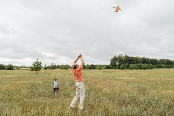 Grandfather and grandson fly a kite on the field. Rural area, Russia. - Foto, afbeelding