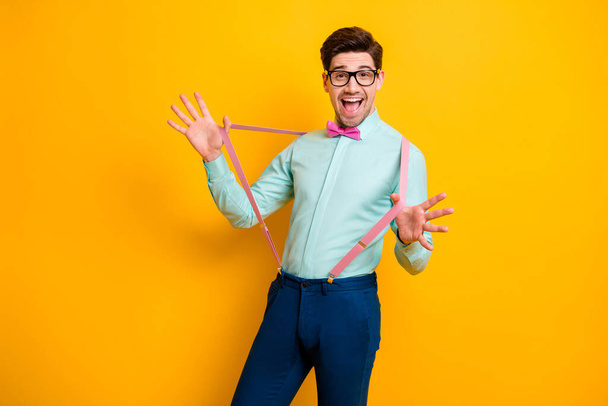 Photo of handsome cool clothes guy boyfriend hands hold stretch pink suspenders beaming smile festive mood wear specs shirt bow tie trousers isolated yellow color background - Foto, Imagem