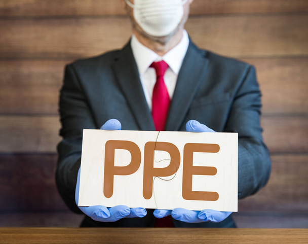 PPE Koncepce podnikatele, lékaře nebo zaměstnavatele v modrých, chirurgických rukavicích a obličejové masce a skládání skládačky s písmeny PPE k vyřešení globálního nedostatku ppe - Fotografie, Obrázek