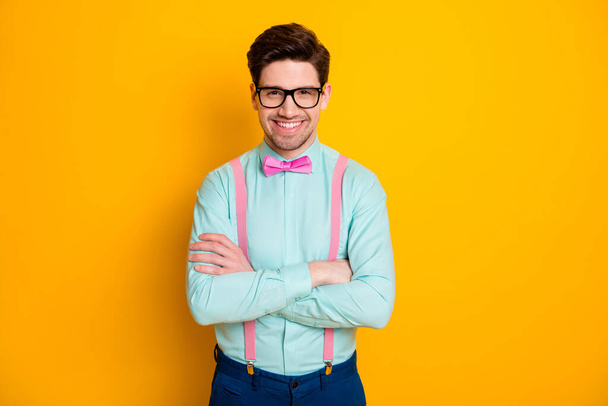 Photo of handsome cool clothes business guy stand self-confidently hands crossed beaming smile wear specs shirt suspenders bow tie trousers isolated yellow color background - Foto, afbeelding