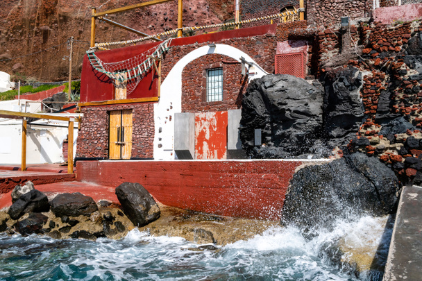 salpicadura de agua del mar Egeo cerca del edificio rojo en la isla griega
  - Foto, imagen