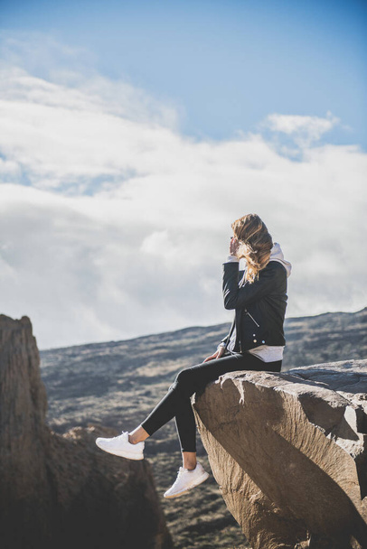 Woman sitting on the edge of a rock looking out into a canyon. Tenerife - Zdjęcie, obraz