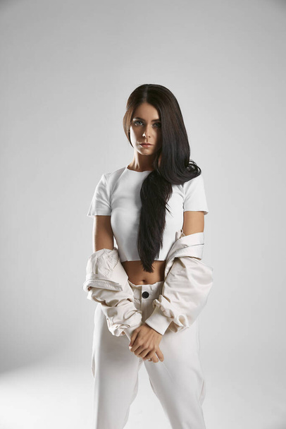 Girl with dark long hair in white sportswear for dancing is smiling on a white, light gray background. Concentrated, serious, fashion - Valokuva, kuva