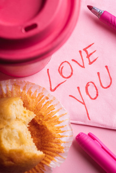 Je t'aime texte écrit sur une serviette en papier près d'une tasse de café rose et un muffin mordu. Message romantique écrit sur une serviette rose
 - Photo, image