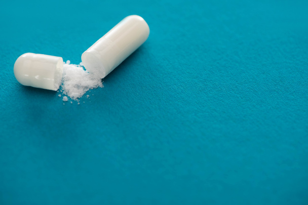 close-up zicht op probiotische capsule met wit poeder op blauwe achtergrond - Foto, afbeelding