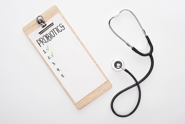 bovenaanzicht van klembord met probiotica lege lijst en stethoscoop op witte achtergrond - Foto, afbeelding
