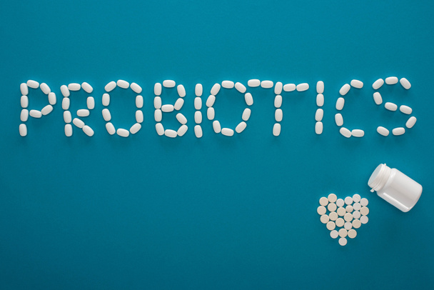 top view of probiotics lettering and heart made of pills and container on blue background - Photo, Image