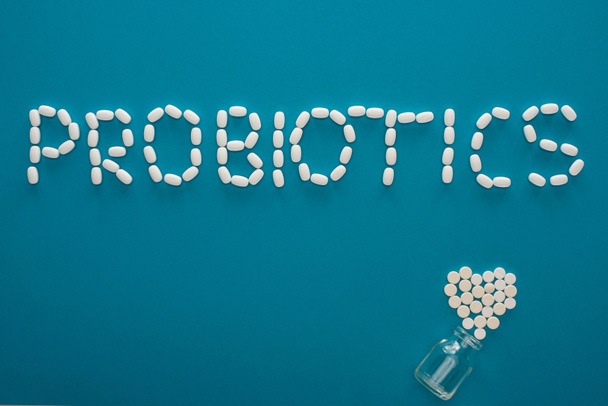 bovenaanzicht van probiotica belettering en hart gemaakt van pillen in de buurt van glazen pot op blauwe achtergrond - Foto, afbeelding